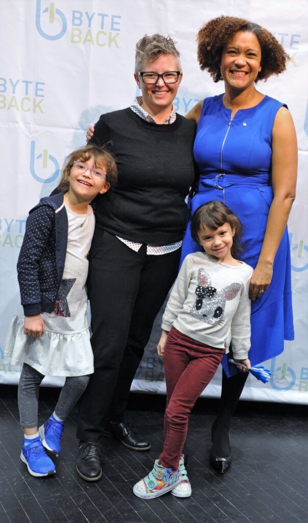 A family of two women standing with two small children in front of them