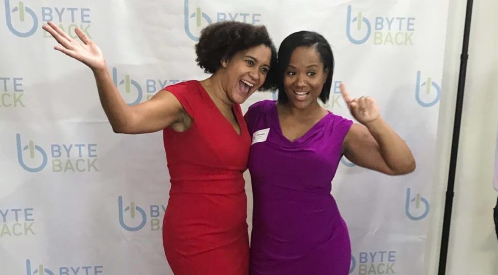 Two women pose smiling in front of a Byte Back logo backdrop